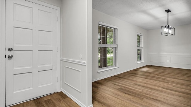 unfurnished dining area featuring wood finished floors, a wainscoted wall, and a chandelier