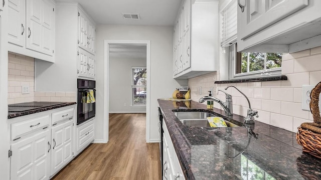 kitchen with black appliances, a sink, white cabinetry, decorative backsplash, and light wood-style flooring