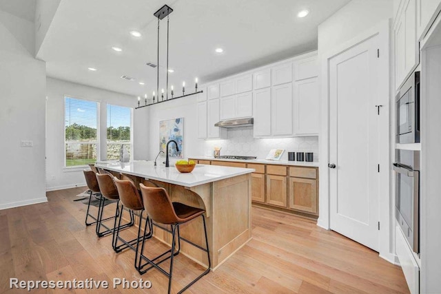 2418 Plumeria, Celina, TX 75009 - kitchen with appliances with stainless steel finishes, light wood finished floors, tasteful backsplash, a breakfast bar area, and light countertops