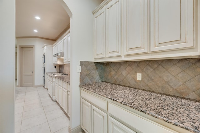 2137 Langdon Dr, Frisco, TX 75033 - kitchen with arched walkways, backsplash, light tile patterned floors, light stone countertops, and under cabinet range hood