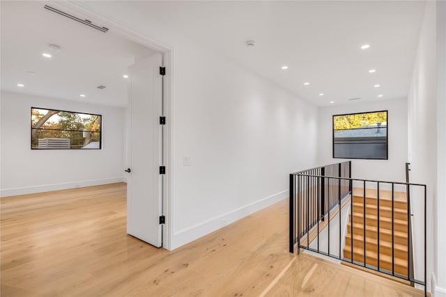 hallway featuring light wood finished floors, an upstairs landing, baseboards, and recessed lighting