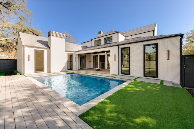 rear view of property with an outdoor pool, brick siding, and a chimney