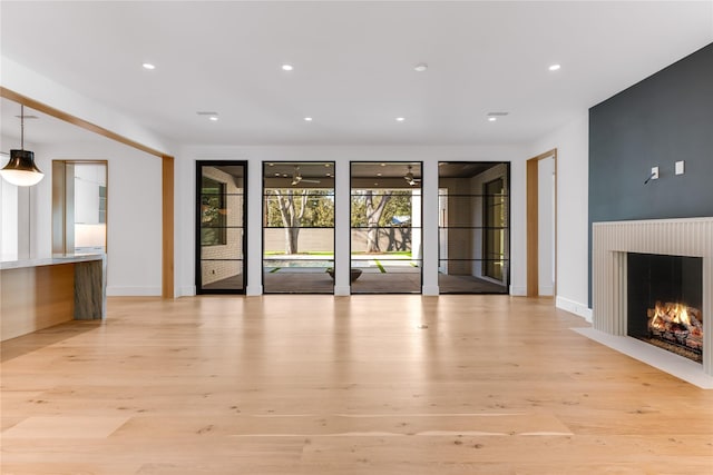 unfurnished living room featuring light wood-style flooring, recessed lighting, and a warm lit fireplace