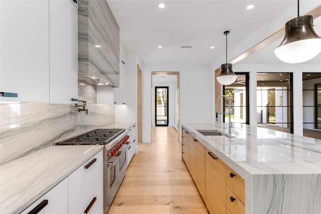 kitchen with modern cabinets, a sink, double oven range, custom range hood, and light brown cabinets