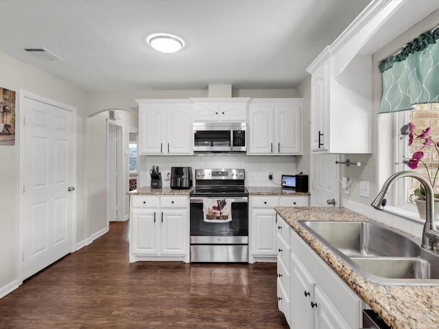 kitchen featuring stainless steel appliances, a sink, arched walkways, white cabinets, and dark wood-type flooring