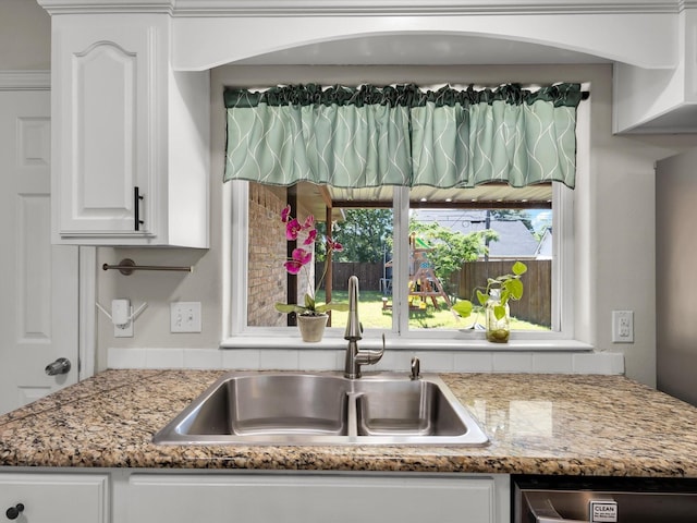 kitchen with a sink, white cabinets, stainless steel dishwasher, and light stone countertops