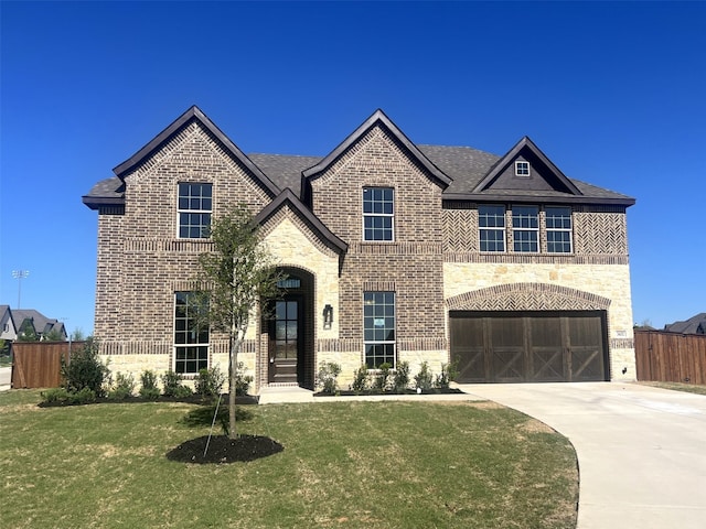 french country home with stone siding, driveway, brick siding, an attached garage, and a shingled roof