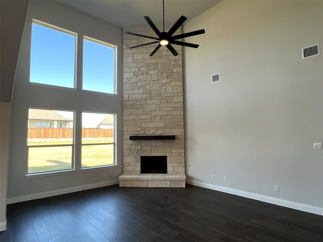 unfurnished living room with ceiling fan, a high ceiling, baseboards, dark wood finished floors, and a fireplace