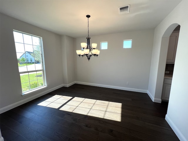 empty room featuring arched walkways, healthy amount of natural light, dark wood finished floors, and baseboards