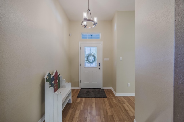 foyer entrance with wood finished floors, a chandelier, and baseboards