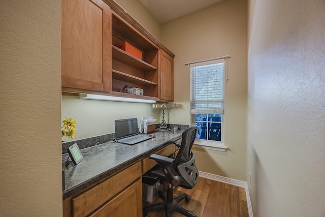 office area featuring built in desk, wood finished floors, baseboards, and a textured wall