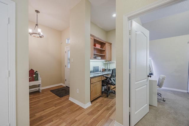 office space featuring light wood finished floors, built in desk, baseboards, and a chandelier