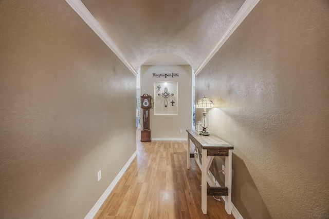 hall featuring light wood-type flooring, baseboards, a textured wall, lofted ceiling, and ornamental molding