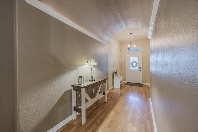 foyer with a textured wall, wood finished floors, baseboards, a chandelier, and a textured ceiling