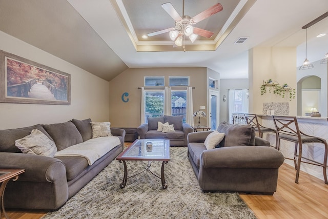 living area with a tray ceiling, light wood-style flooring, ceiling fan, and arched walkways