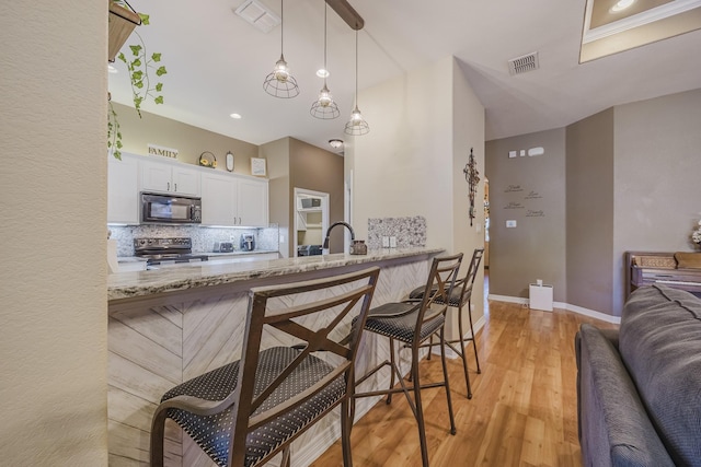 kitchen featuring black microwave, stainless steel electric stove, a breakfast bar, and light stone countertops