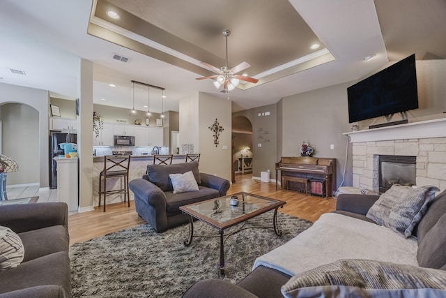 living area featuring a tray ceiling, arched walkways, light wood-style flooring, a ceiling fan, and recessed lighting