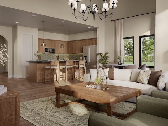 living room with a towering ceiling, light wood finished floors, a chandelier, recessed lighting, and arched walkways