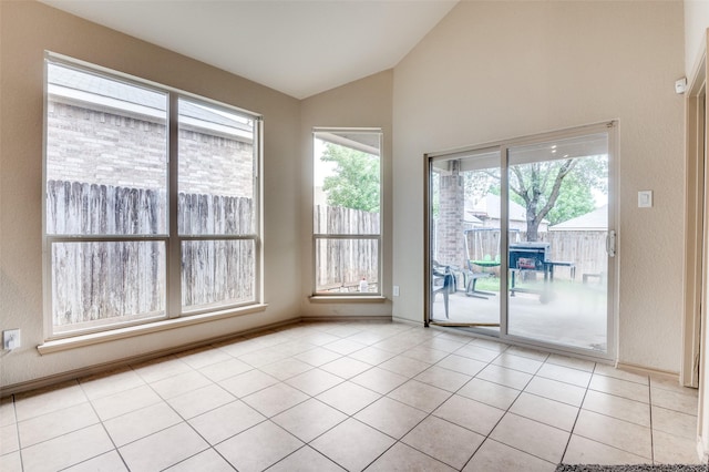 spare room with lofted ceiling, plenty of natural light, light tile patterned floors, and baseboards