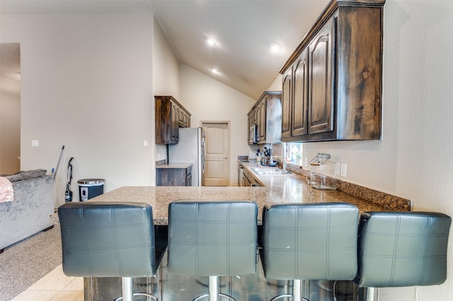 kitchen with dark brown cabinetry, stainless steel appliances, lofted ceiling, a peninsula, and a sink