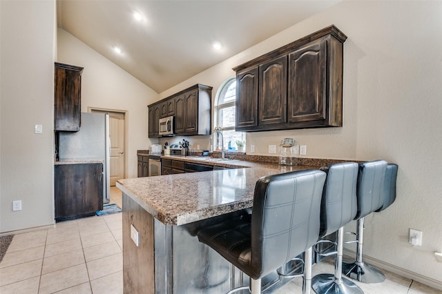 kitchen with stainless steel appliances, dark brown cabinetry, lofted ceiling, a kitchen breakfast bar, and a sink