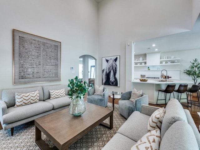living area with arched walkways, wood finished floors, a high ceiling, and recessed lighting