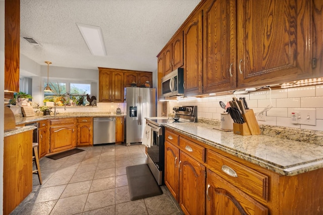 2608 Rivercrest Dr, Arlington, TX 76006 - kitchen featuring appliances with stainless steel finishes, brown cabinetry, decorative backsplash, decorative light fixtures, and light stone countertops