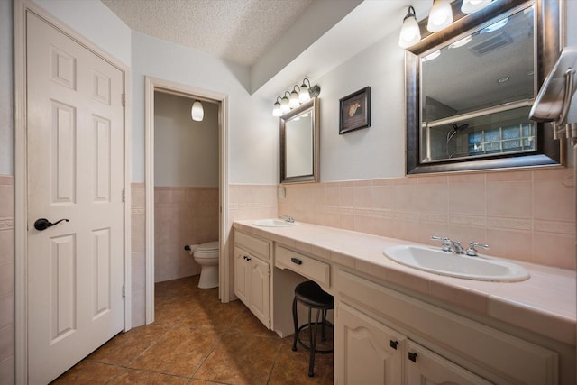 2608 Rivercrest Dr, Arlington, TX 76006 - full bathroom featuring toilet, tile walls, double vanity, a textured ceiling, and tile patterned flooring