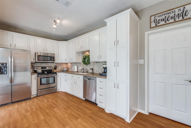 kitchen with stainless steel appliances, light wood-style flooring, decorative backsplash, and white cabinets