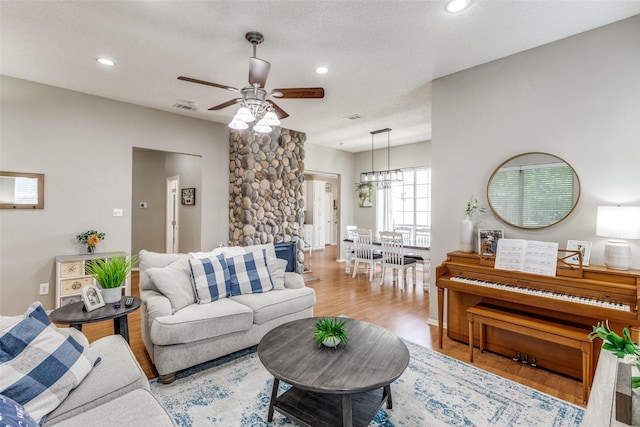 living area featuring light wood finished floors, a ceiling fan, recessed lighting, a textured ceiling, and a chandelier