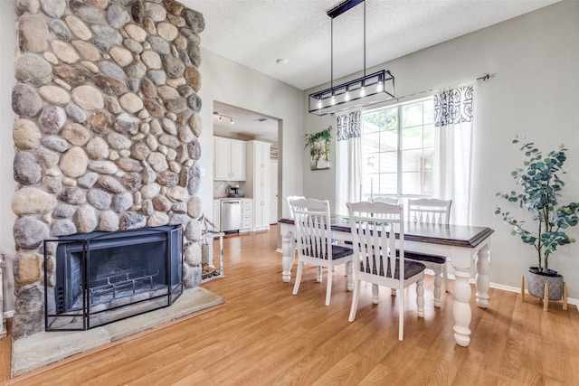 dining area with light wood-style floors, a textured ceiling, a fireplace, and baseboards