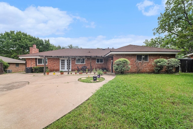 ranch-style house featuring a tile roof, central air condition unit, a front yard, a chimney, and brick siding