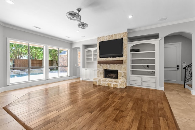 unfurnished living room with wood finished floors, ornamental molding, a fireplace, baseboards, and arched walkways