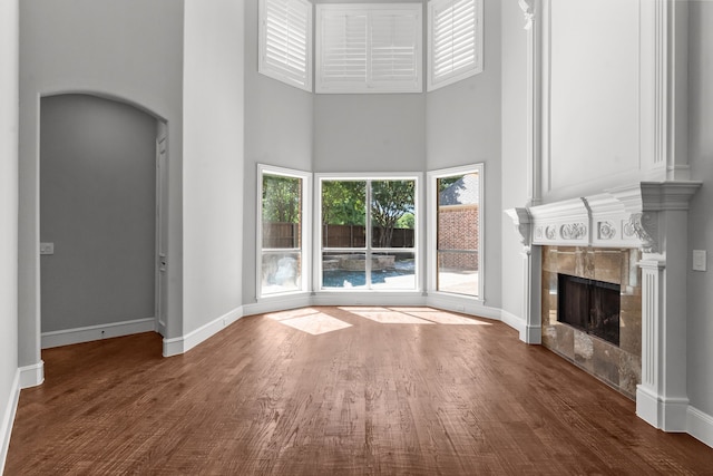 unfurnished living room with a high ceiling, a high end fireplace, wood finished floors, and baseboards