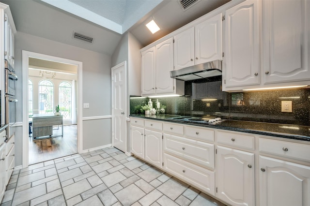 3336 Sage Brush Trl, Plano, TX 75023 - kitchen with dark countertops, under cabinet range hood, backsplash, white cabinetry, and lofted ceiling