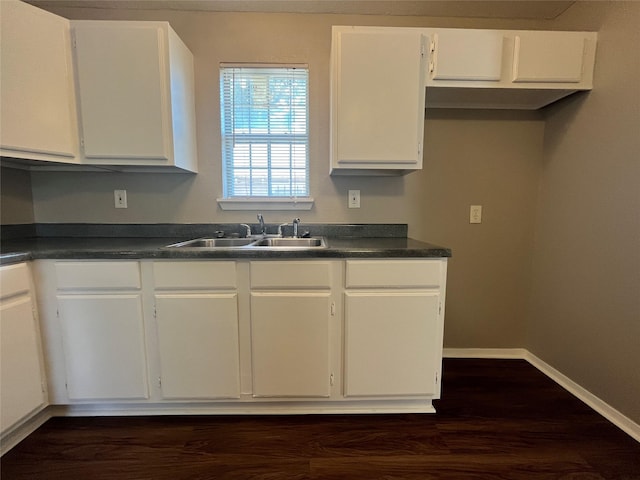 kitchen with a sink, dark countertops, white cabinets, and baseboards