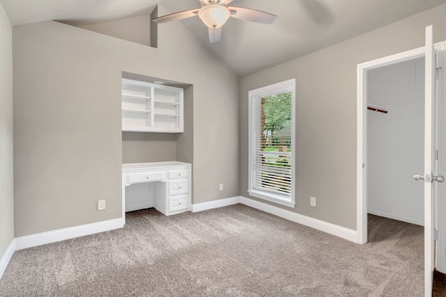 unfurnished bedroom with a walk in closet, carpet, baseboards, and vaulted ceiling