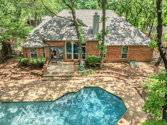 rear view of house featuring roof with shingles, brick siding, a chimney, french doors, and a patio