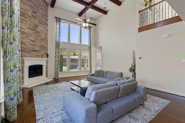living room featuring beamed ceiling, a ceiling fan, wood finished floors, a high ceiling, and a large fireplace