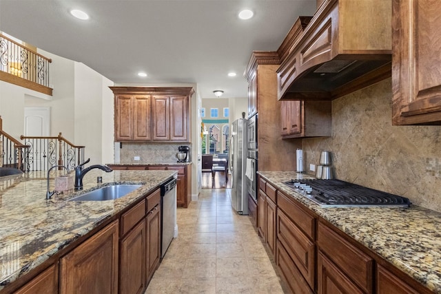 kitchen with a sink, custom range hood, stainless steel appliances, backsplash, and light stone countertops