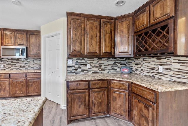 1717 Adams Ln, Azle, TX 76020 - kitchen with stainless steel microwave, backsplash, light stone countertops, light wood-style flooring, and dark brown cabinets