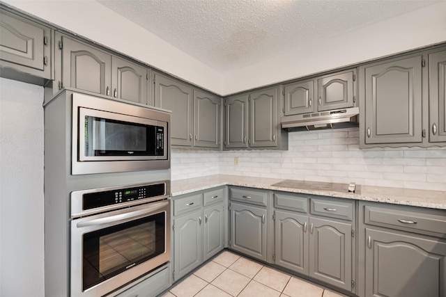 kitchen featuring appliances with stainless steel finishes, under cabinet range hood, gray cabinets, a textured ceiling, and tasteful backsplash