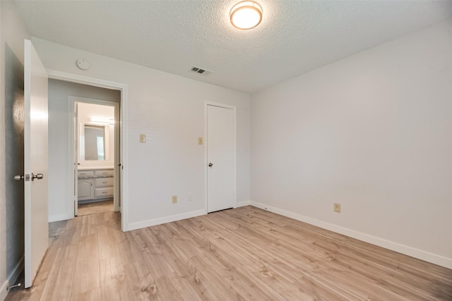 unfurnished bedroom with light wood-type flooring, baseboards, a textured ceiling, and a closet