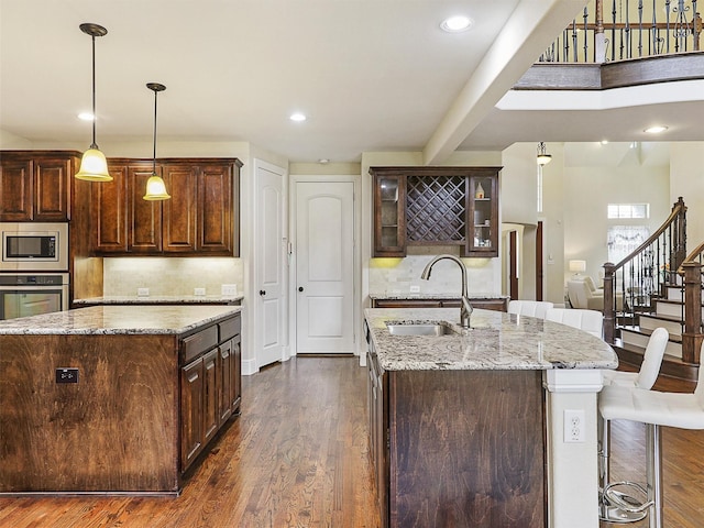 2165 Hidalgo Ln, Frisco, TX 75034 - kitchen featuring a sink, appliances with stainless steel finishes, a kitchen island with sink, backsplash, and dark wood-style floors