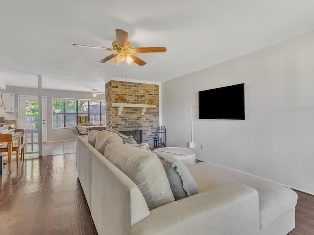 living area with a ceiling fan, wood finished floors, and a brick fireplace