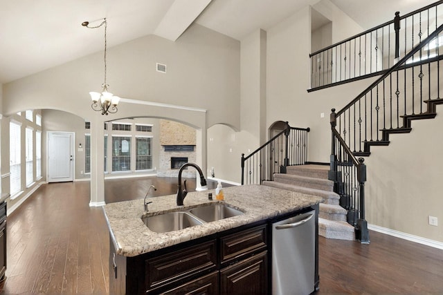kitchen featuring a sink, arched walkways, open floor plan, stainless steel dishwasher, and hanging light fixtures