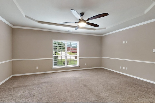 carpeted empty room featuring a raised ceiling, a ceiling fan, ornamental molding, and baseboards