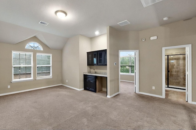 unfurnished living room featuring light carpet, baseboards, lofted ceiling, and a sink
