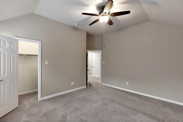 unfurnished bedroom featuring vaulted ceiling, a walk in closet, carpet, a ceiling fan, and baseboards