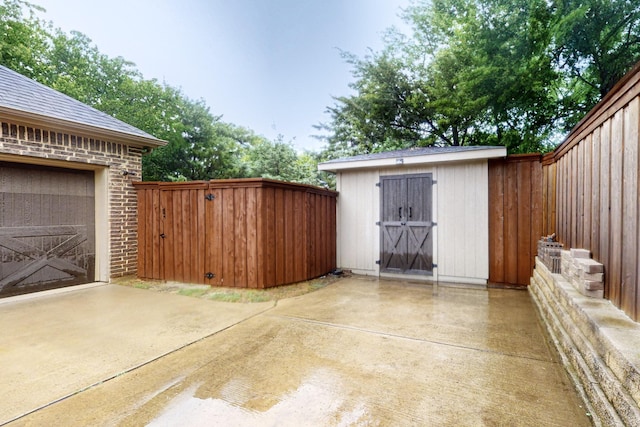 view of patio / terrace with a shed, an outdoor structure, fence, driveway, and a garage
